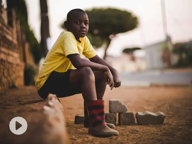 a video of a boy wearing a yellow t-shirt and sitting beside road